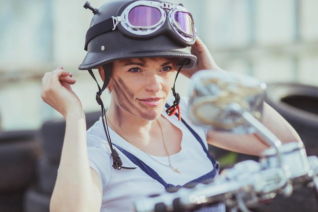 Mädchen-Automechaniker in einem Helm schaut in einen Motorradspiegel