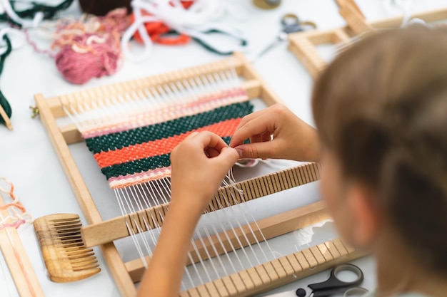 Mädchen beim Weben eines kleinen Teppichs mit Muster in der Meisterklasse zum Thema Weben Mädchen studiert, wie man auf einem manuellen Tischwebstuhl webt Prozess der Erstellung Handgefertigtes Konzept
