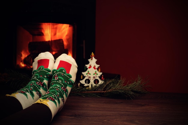 Mädchen Beine in Socken in der Nähe des Kamins mit einem kleinen Weihnachtsbaum Winterurlaub Konzept Gemütliche entspannte magische Atmosphäre