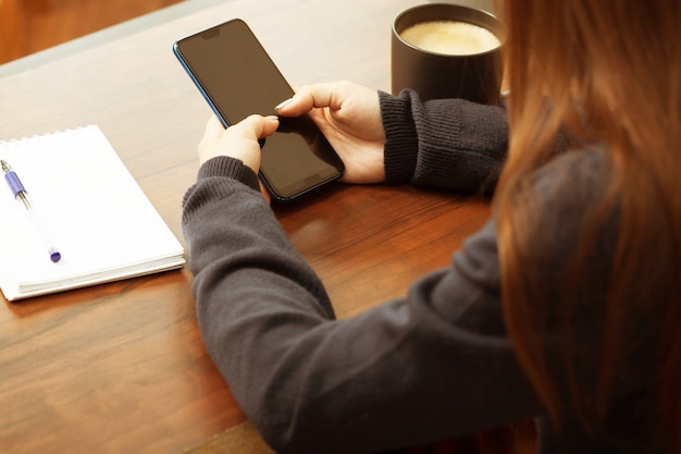 Mädchen benutzt das Telefon am Tisch, schaut sich Nachrichten, Post, Geschäftskonzept an