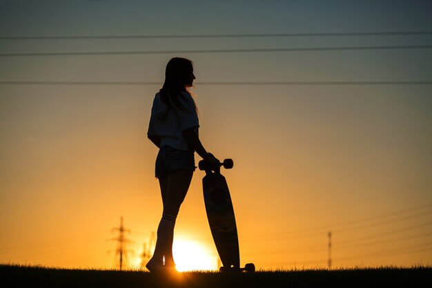 Mädchen betrachtet den Sonnenuntergang, der ein longboard in ihrer Hand hält