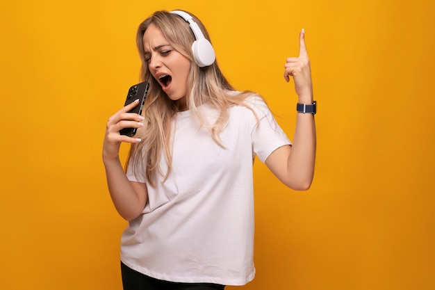 Mädchen bricht zu Musik in Kopfhörern ab, die ein Telefon in ihren Händen auf einem gelben Studiohintergrund halten