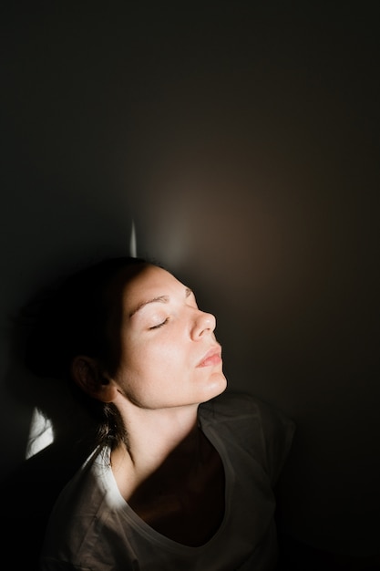 Mädchen, das allein in der Sonnenlichttasche im dunklen Raum sitzt. Konzept der psychischen Gesundheit