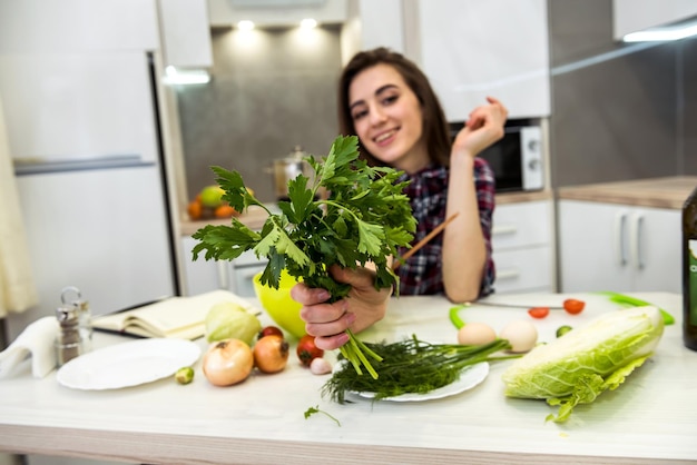 Mädchen, das an einem Küchentisch posiert, während es einen Salat aus verschiedenen Gemüsen und Grüns für einen gesunden Lebensstil zubereitet