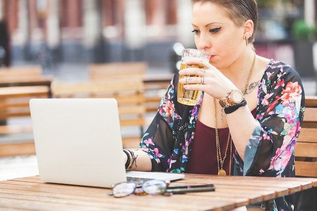 Mädchen, das an ihrem Computer arbeitet und Bier trinkt