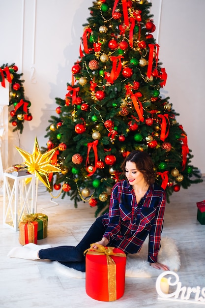 Mädchen, das auf einem Boden nahe einem Weihnachtsbaum und einem großen Geschenk sitzt und zur Seite schaut