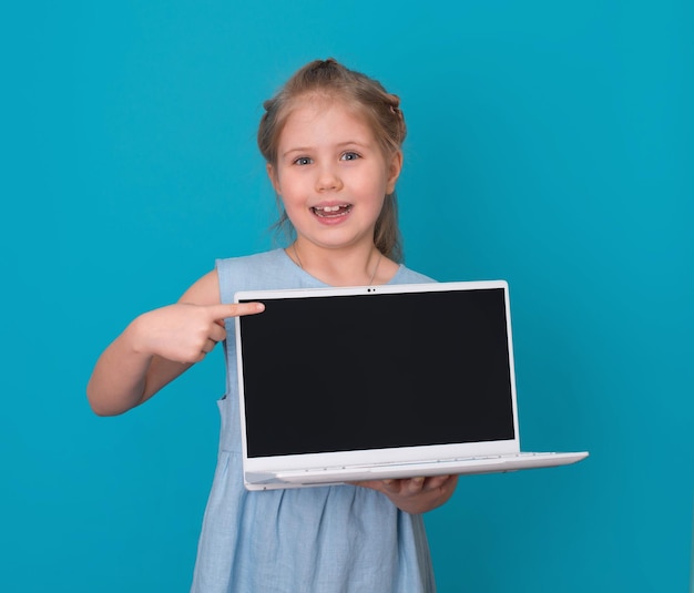 Mädchen, das auf leeren Laptopbildschirm über blauem Hintergrund zeigt