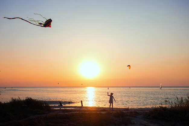 Mädchen, das bei Sonnenuntergang einen Drachen auf dem Meer fliegt