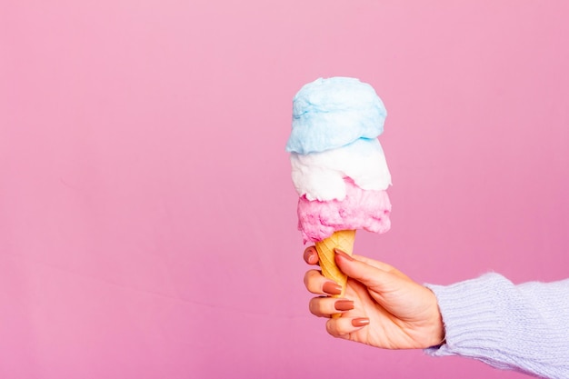 Mädchen, das blauen Pullover und Jeans trägt und ein Zuckerwatte-Eis hält. Hellrosa Hintergrund.