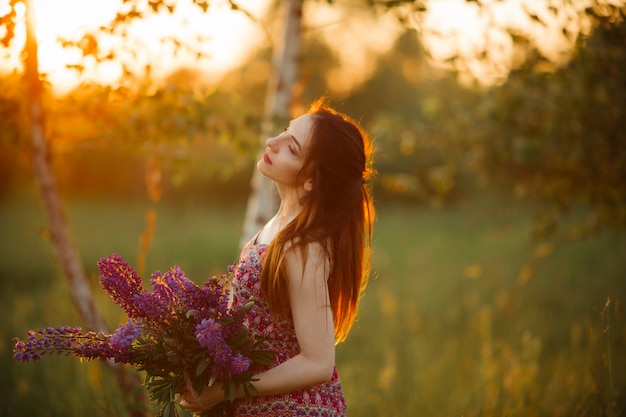 Mädchen, das Blumen hält. Brünette im Feld. Sonnenuntergang