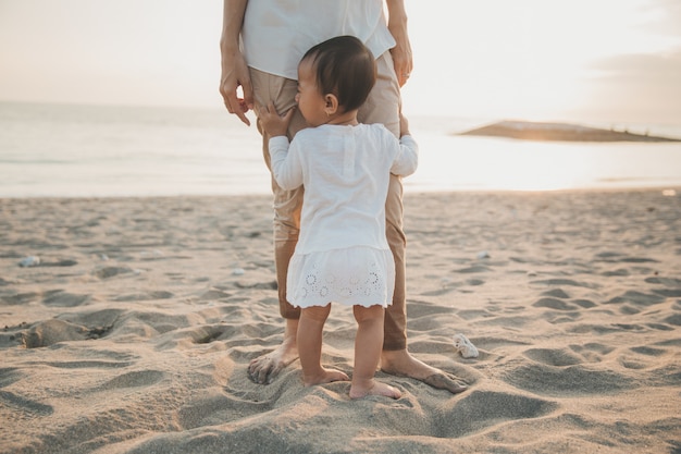 Mädchen, das das Bein der Mutter beim Stehen auf dem Strand hält