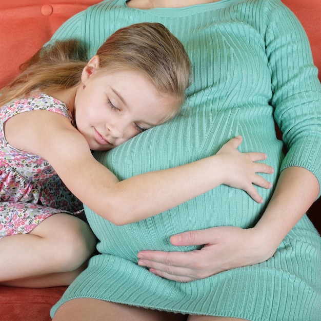 Mädchen, das den Bauch der schwangeren Mutter umarmt