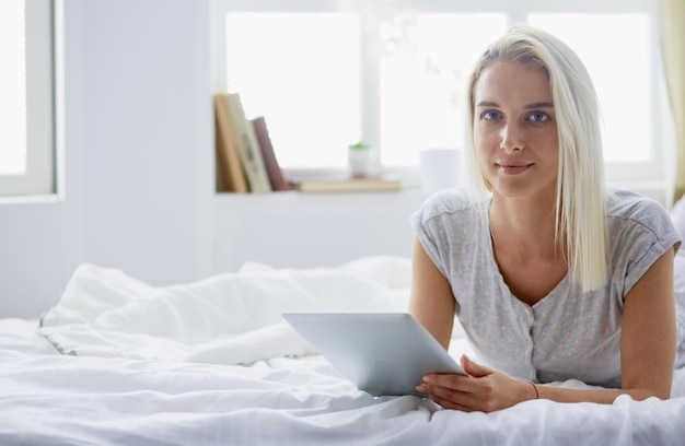 Mädchen, das digitales Tablet mit leerem Bildschirm hält und im Schlafzimmer in die Kamera lächelt