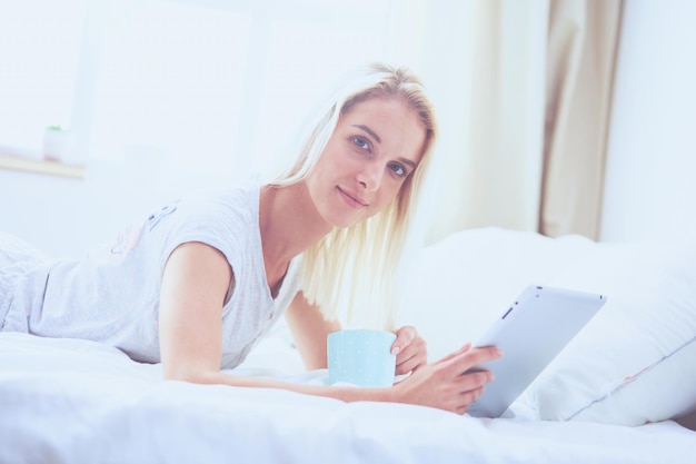 Mädchen, das digitales Tablet mit leerem Bildschirm hält und im Schlafzimmer in die Kamera lächelt