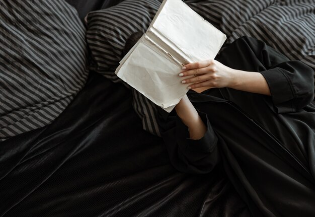 Mädchen, das ein Buch liest, während im Bett in einer Draufsicht von oben liegen.