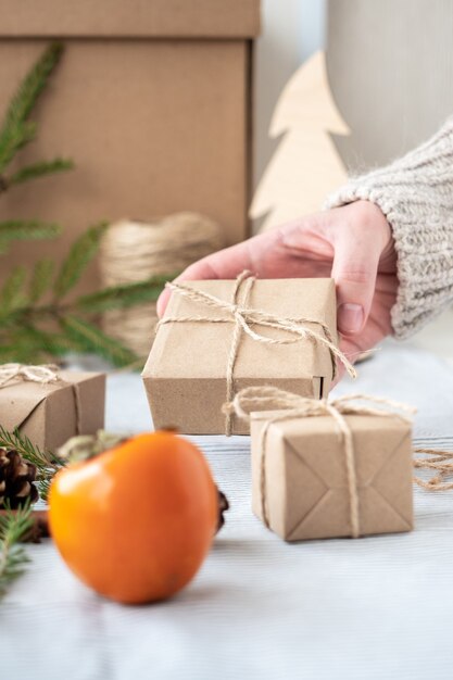 Mädchen, das ein Geschenk hält, verpackt mit ihren eigenen Händen, Nahaufnahme. Weihnachtsdekoration, Design einer Geschenkbox für Weihnachten aus natürlichen Materialien. Neujahrsatmosphäre, Vorbereitung auf Weihnachten.