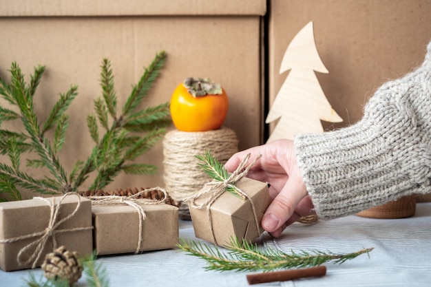 Mädchen, das ein Geschenk hält Verpackt mit ihren eigenen Händen, Nahaufnahme. Weihnachtsdekoration, Gestaltung einer Geschenkbox zu Weihnachten aus natürlichen Materialien. Neujahrsstimmung, Vorbereitung auf Weihnachten.