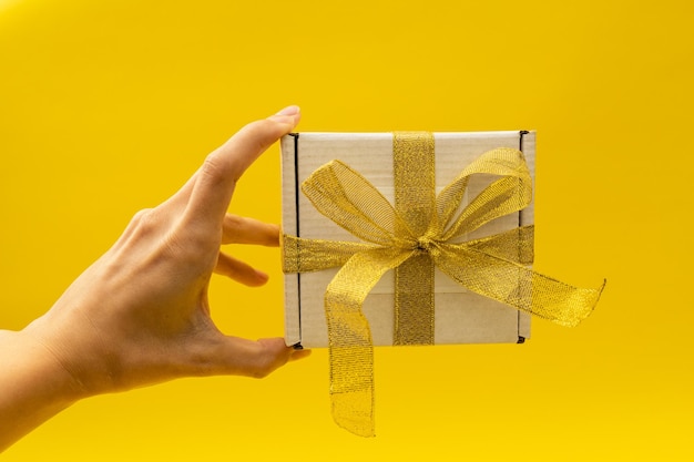 Mädchen, das ein Neujahrsgeschenk in einem weißen Kasten mit einem goldenen Band auf einem gelben Hintergrund hält