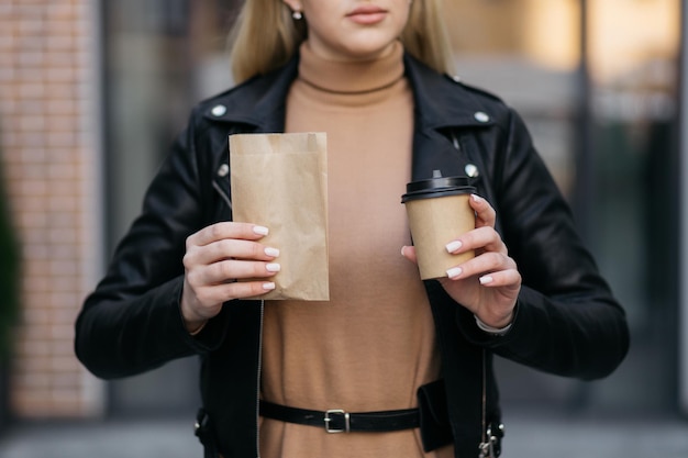 Mädchen, das ein Paket von Croissants und Kaffee auf dem Hintergrund des Einkaufszentrums hält Schönes Mädchen im Stadtzentrum Croissant im Paket Kaffee in den Händen