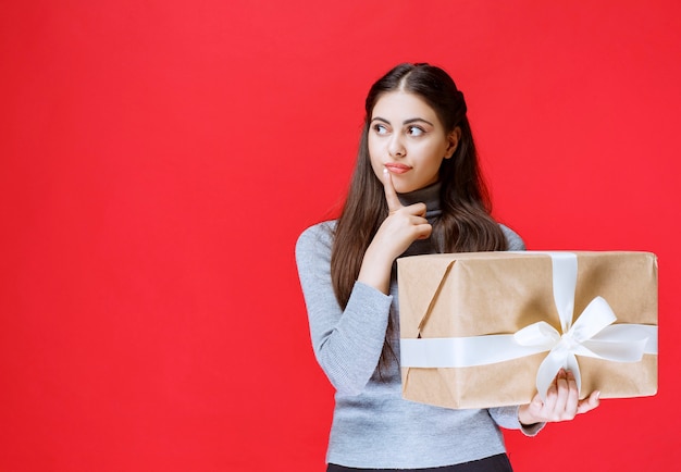 Mädchen, das eine Pappgeschenkbox hält und denkt.