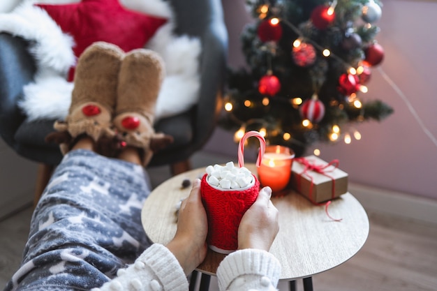 Mädchen, das eine rote Tasse mit Kakao und Marshmallows in den Händen hält, gemütlicher Weihnachtsmorgen