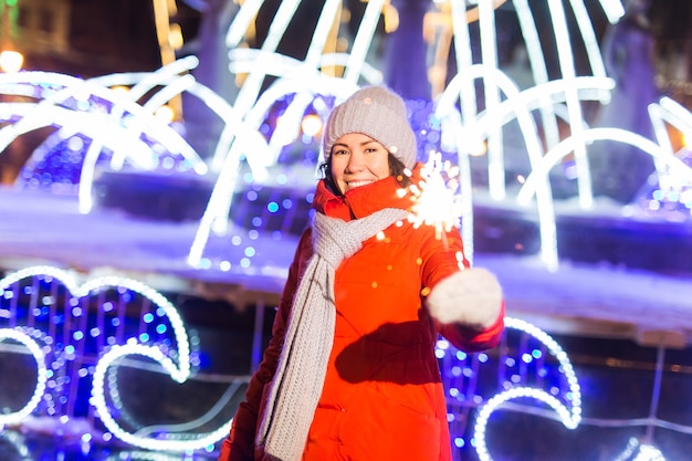 Mädchen, das eine Wunderkerze in der Hand hält Winterstadthintergrund-Schneeflocken im Freien