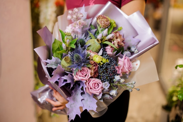 Mädchen, das einen Blumenstrauß von Rosen, getrockneten Mohnblumen und lila Blättern hält