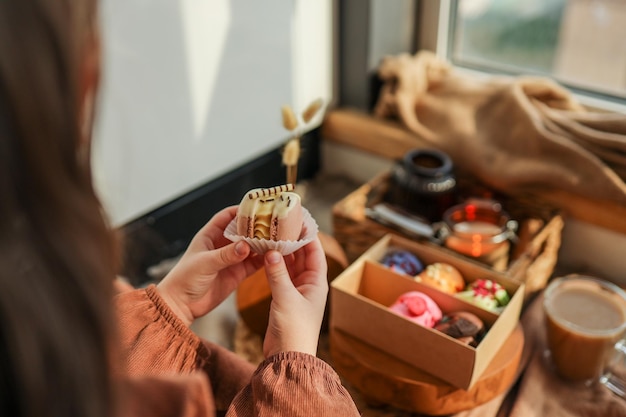 Mädchen, das einen Macaron in der Hand hält, mit einer Schachtel mit verschiedenen Macarons im Hintergrund in einer gemütlichen häuslichen Atmosphäre