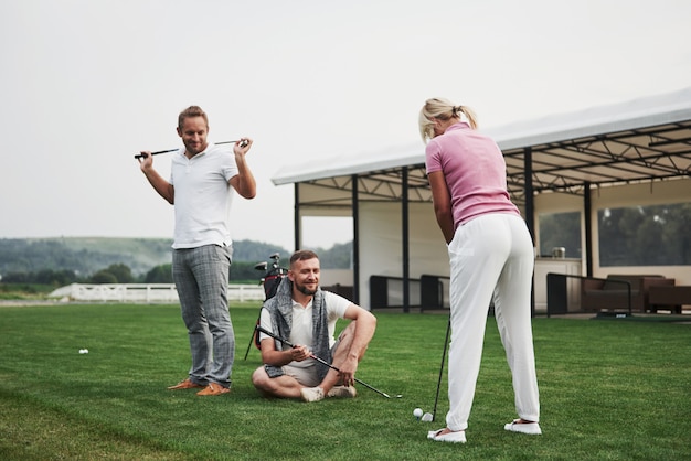 Mädchen, das Golf spielt und durch Putter auf Grün schlägt. Ihre Lehrerin hilft, die Technik zu erforschen und ihre ersten Schläge zu machen