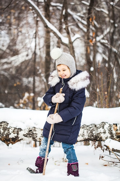 Mädchen, das im Winterwald in einer blauen Jacke und im grauen Hut geht