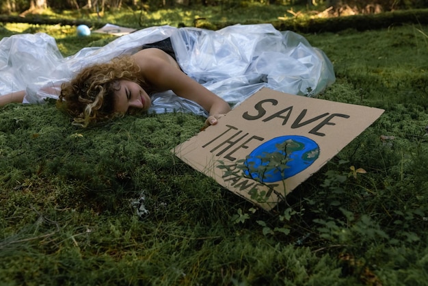 Mädchen, das in der Hand eine Pappfahne hält. Das Mädchen ist in Plastikfolie eingewickelt. Schütze die Umwelt