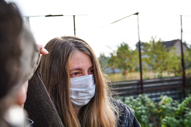 Mädchen, das medizinische Maske wegen Luftverschmutzung oder Virusepidemie in der Stadt trägt. Frau mit medizinischer und Gesichtsmaske auf einem blauen Himmel.