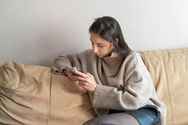 Mädchen, das mit einem Telefon in ihren Händen auf der Couch sitzt