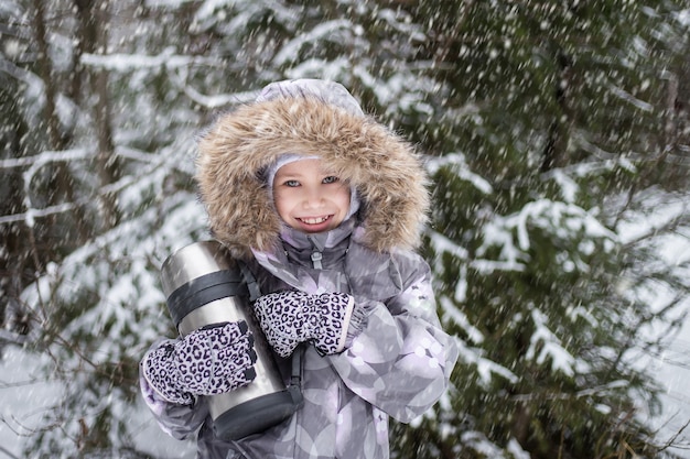 Mädchen, das mit einer Thermoskanne und im Winterwald geht