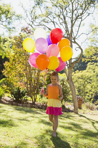 Foto mädchen, das mit lutscher und ballonen im park geht