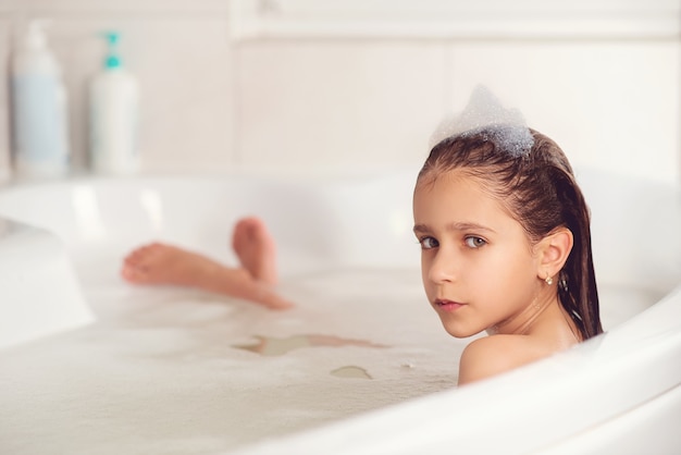 Mädchen, das mit Schaum im Badezimmer badet und spielt