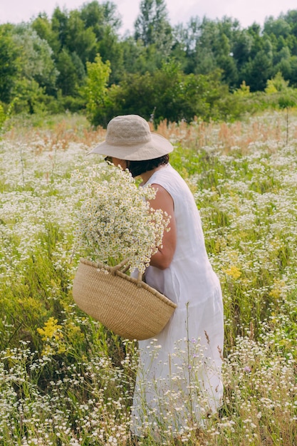 Mädchen, das mitten auf dem Feld einen Strohkorb mit Gänseblümchen hält