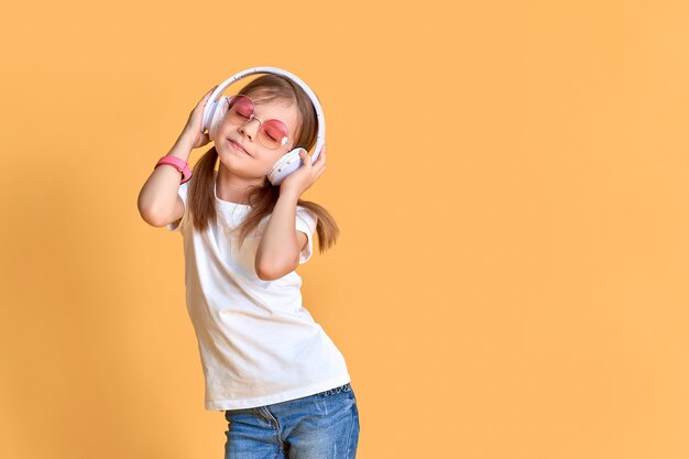 Mädchen, das Musik in den Kopfhörern hört. Nettes Kind, welches die glückliche Tanzmusik, das nahe Auge und die Lächelnaufstellung genießt