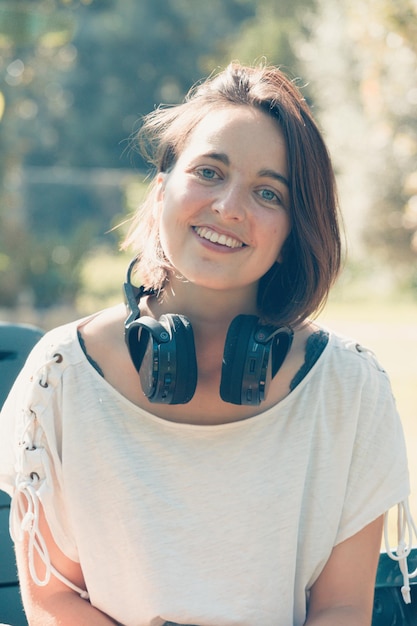 Mädchen, das Musik mit Kopfhörern in einem Park hört, lächelt mit Vergnügen, während sie Musik hört
