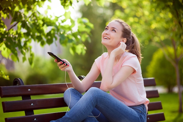 Mädchen, das Musik von einem Mobiltelefon im Park auf einer Bank hört