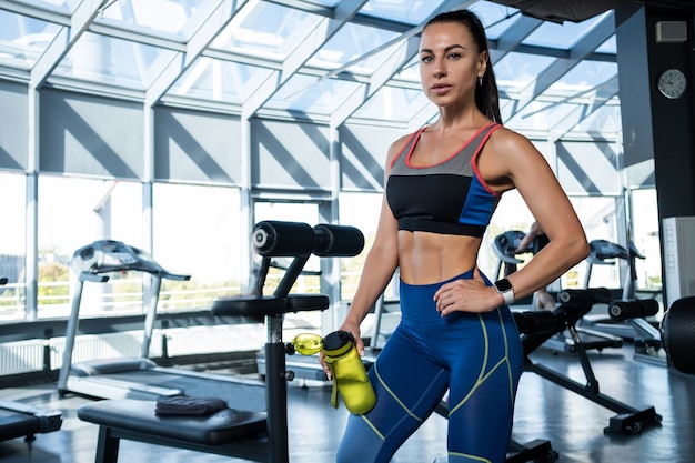 Mädchen, das nach dem Training mit Wasserflasche im Fitnessstudio steht