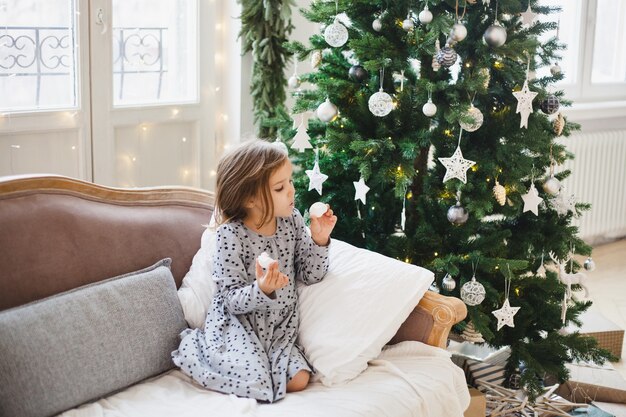 Mädchen, das neben Weihnachtsbaum zu Hause sitzt