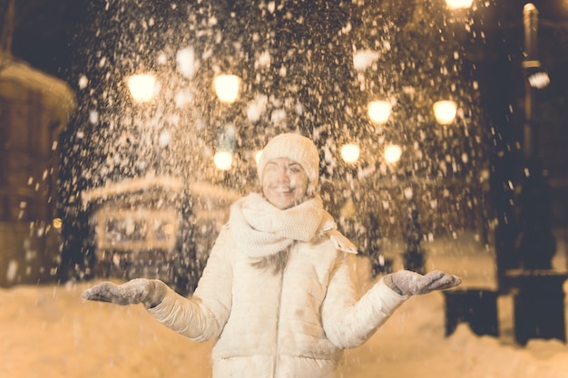 Mädchen, das Spaß auf der Weihnachtsdekoration hat, beleuchtet Straße. Junge glückliche lächelnde Frau, die draußen stilvollen gestrickten Schal und Jacke trägt. Modell lachen. Winterwunderland-Stadtszene, Silvesterparty.