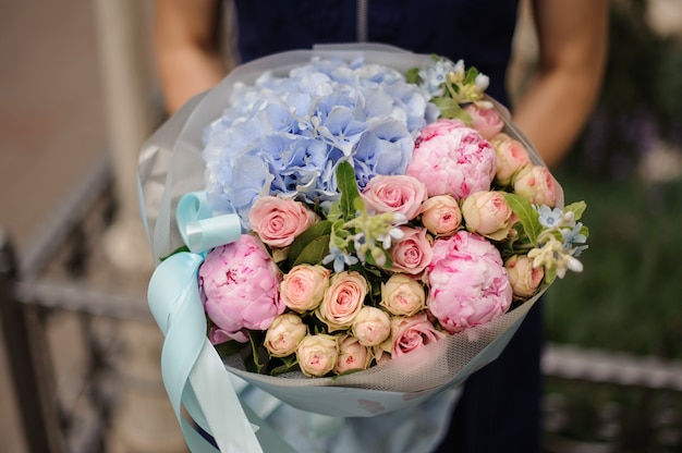 Mädchen, das Strauß der rosa Pfingstrosen und der Rosen und der blauen Hortensie hält