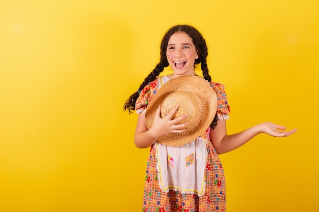 Mädchen, das traditionelle orange Kleidung für festa junina trägt Begrüßung und lächelnder Hut