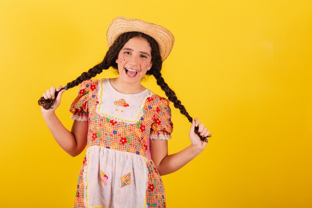 Mädchen, das traditionelle orangefarbene Kleidung für festa junina trägt. Lächelnde Haarzöpfe halten