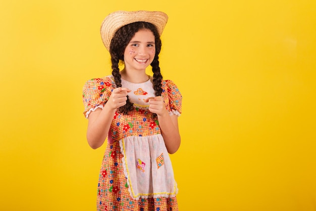 Mädchen, das traditionelle orangefarbene Kleidung für festa junina trägt und mit dem Finger zeigt, was Sie ausgewählt haben