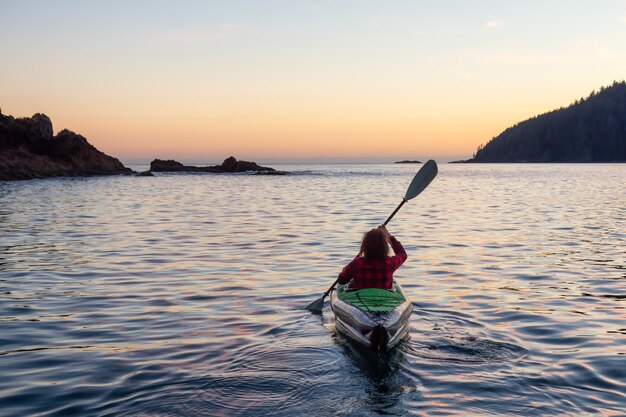 Mädchen, das während eines bewölkten Sommersonnenuntergangs im Pazifischen Ozean Kajak fährt