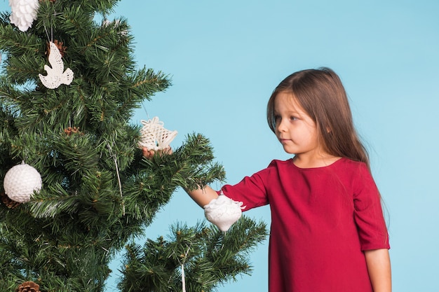 Mädchen, das Weihnachtsbaum mit Spielzeug und Kugeln verziert