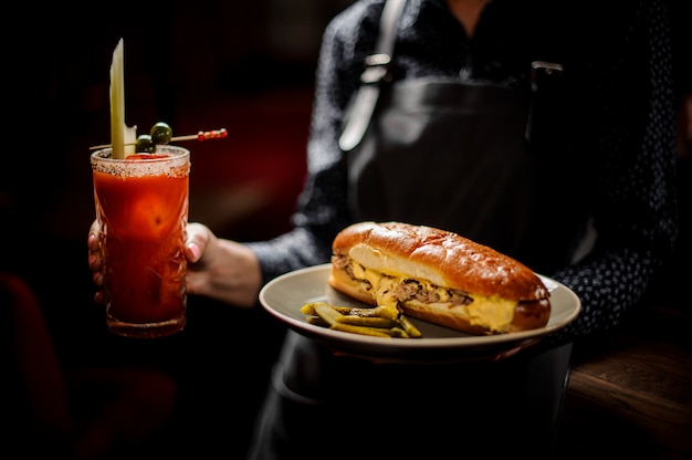 Mädchen, das weißen Teller mit leckerem Fleischsandwich und rotem köstlichem Cocktail hält